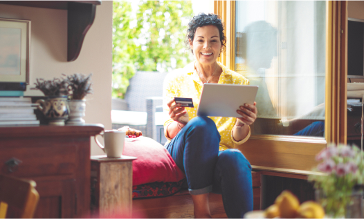 Mature woman sitting by the window, holding a digital tablet and a credit card